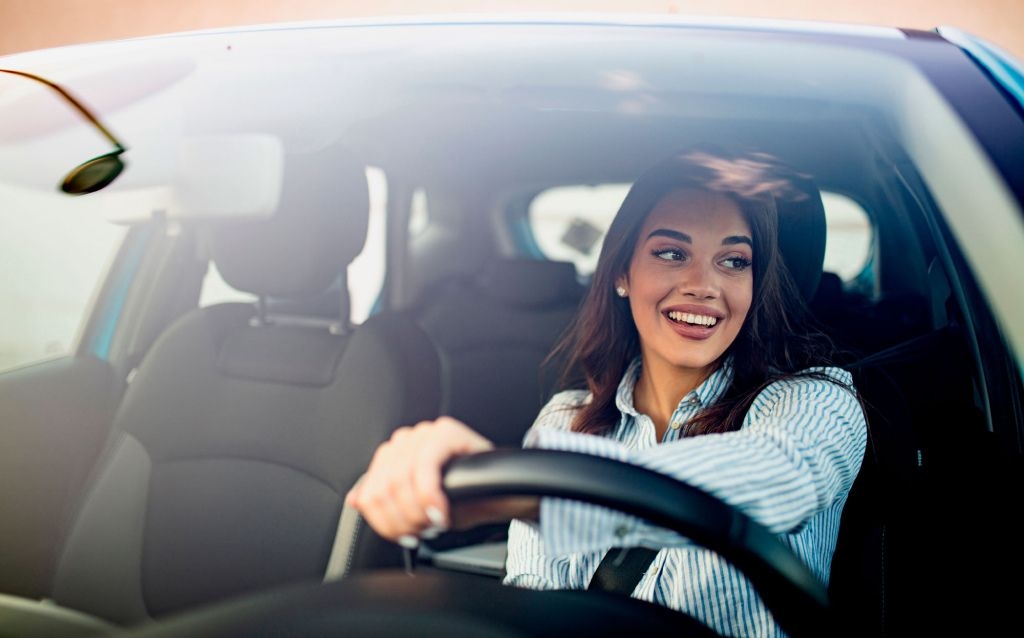 tipos de seguro de carro | mulher dirigindo um veículo, o ângulo da foto tem como foco os bancos da frente