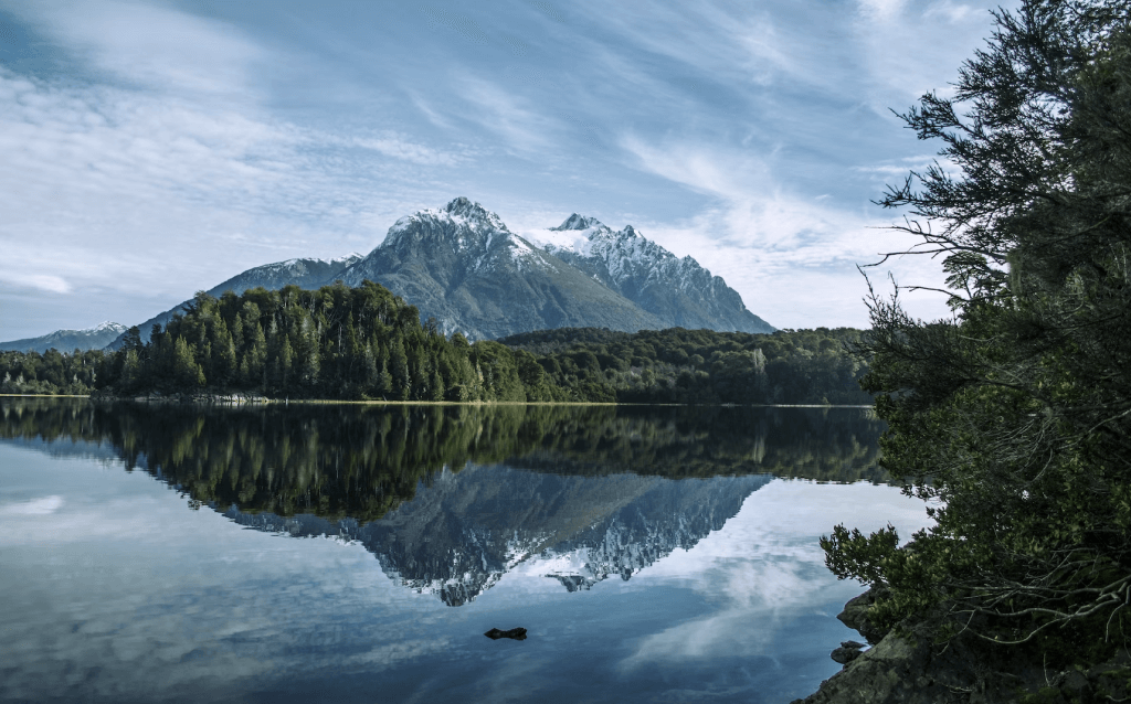 Um lago com florestas ao redor e uma montanha com ponta de neve no fundo da paisagem.