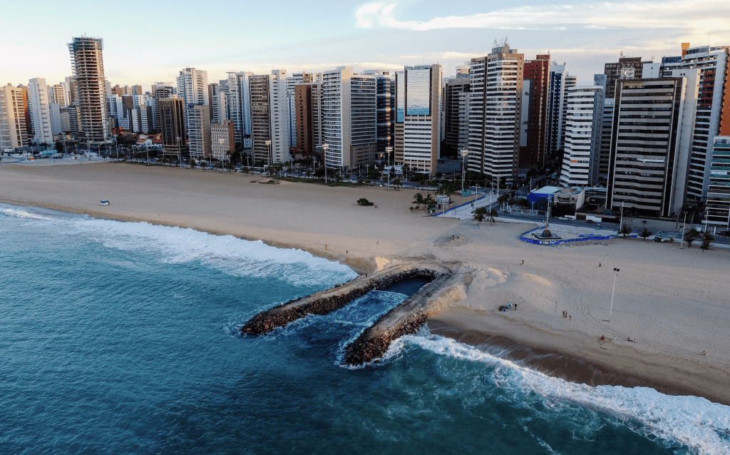 Uma praia de Fortaleza durante o dia com prédios atrás complementando a paisagem.