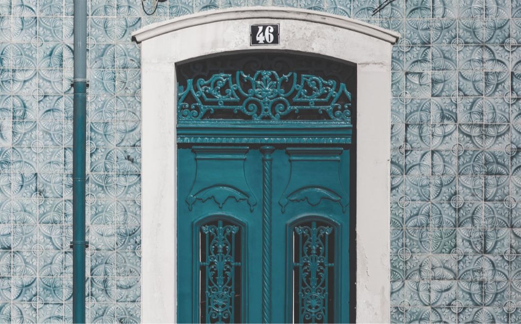 viajar para Portugal | porta grande feita em madeira na cor azul, número 46 acima da porta, a parede é feita de azulejos azuis