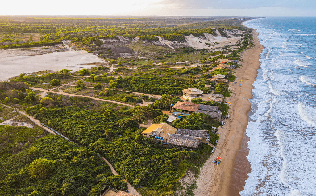 Vista de cima da cidade de Itaúnas. Do lado direito está a areia e o mar, e do esquerdo, as casas de praia, dunas e diversas árvores que completam as paisagens.