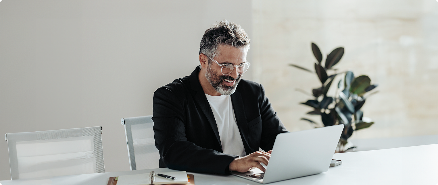 Homem grisalho sorri enquanto trabalha no laptop.