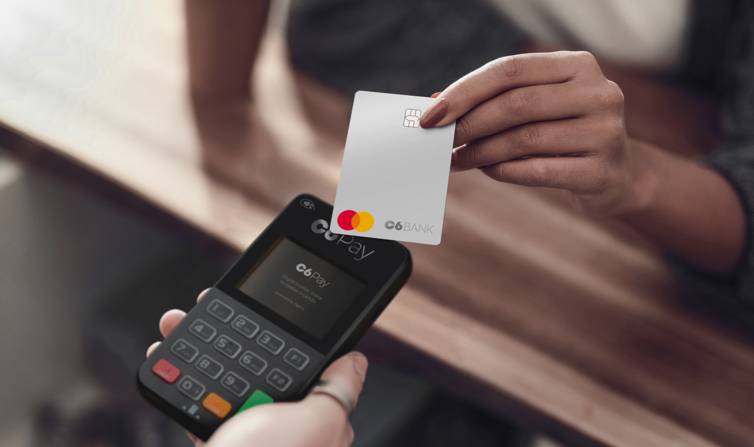 Maquininha C6 Supermini recebendo pagamento por aproximação de uma mulher com cartão C6 Bank Silver.