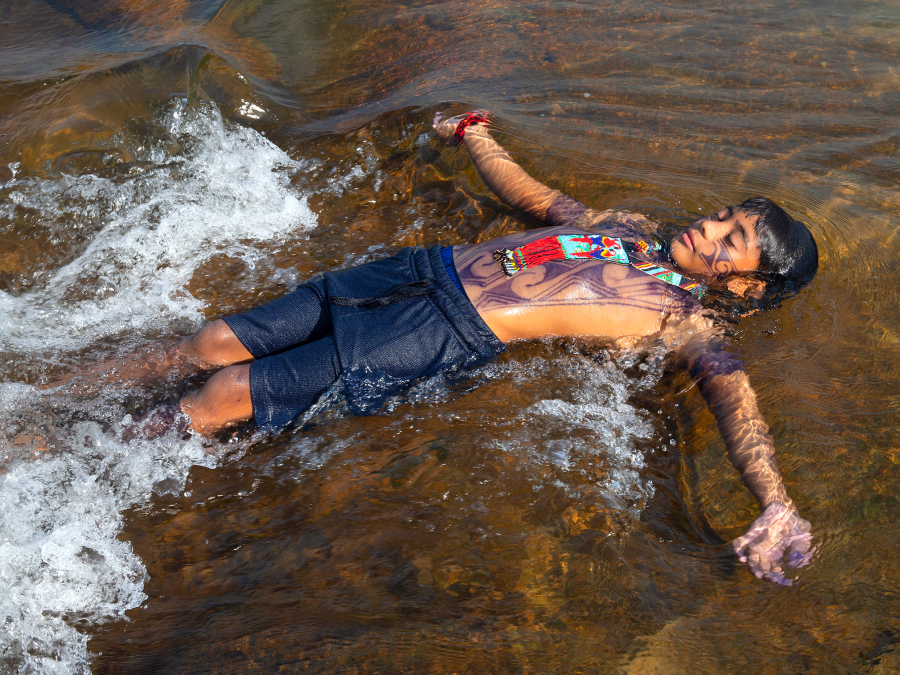 Foto de menino indígena de barriga pra cima em banho de rio.