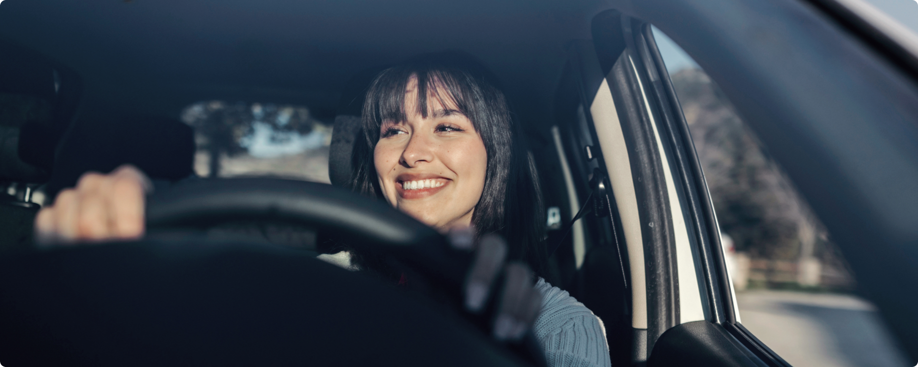 Mulher de cabelos pretos sorrindo e dirigindo um veículo