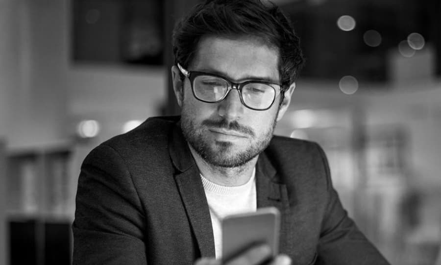 Homem branco sentado olhando para o celular em foto preto e branco