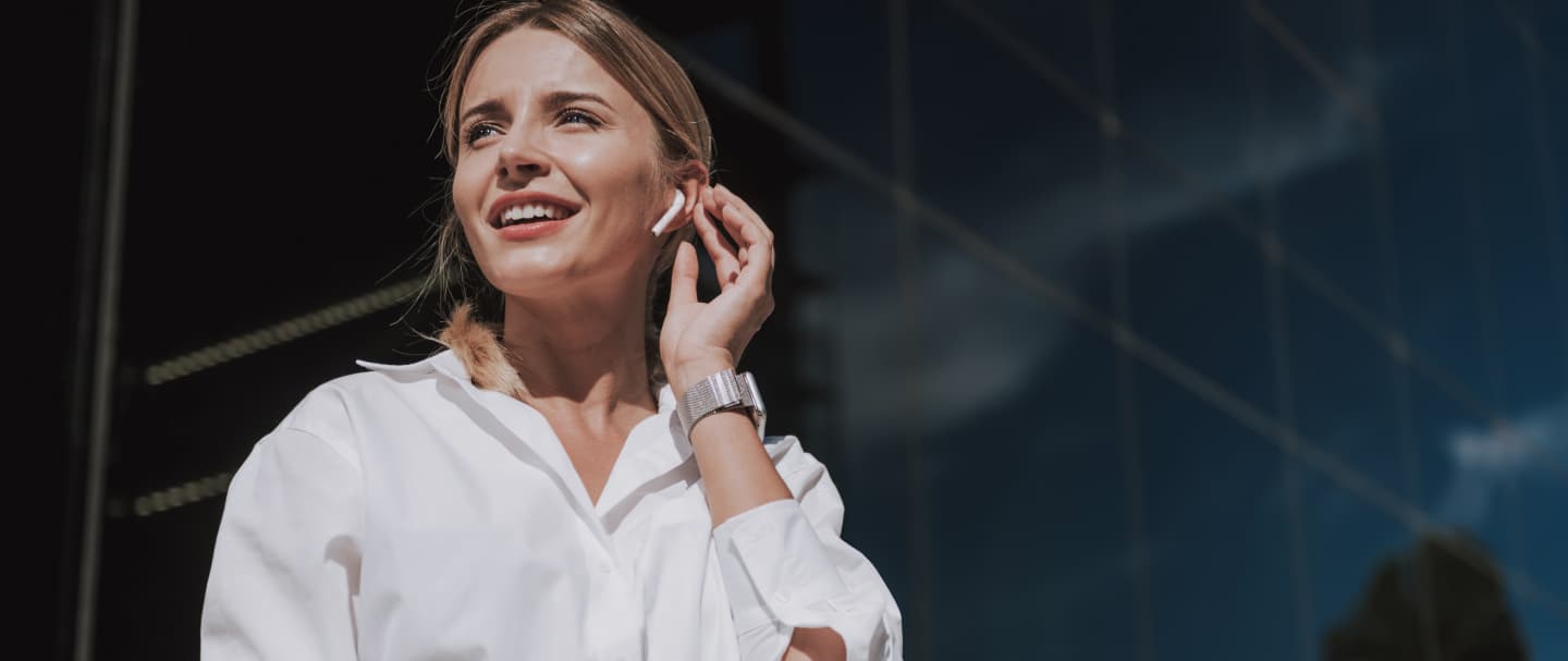 Mulher sorridente com fone de ouvido sem fio, com prédio espelhado ao fundo. Mulher sorridente com fone de ouvido sem fio, com prédio espelhado ao fundo.