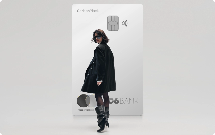 Mulher de preto caminha à frente de um Cartão C6 Carbon Mastercard Black prata em tamanho ampliado, sobre fundo claro.