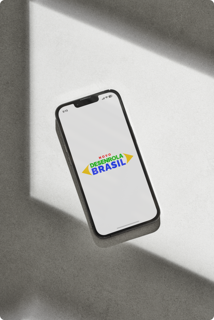 Celular sobre superfície cinza exibe na tela o logotipo colorido do programa Desenrola Brasil.