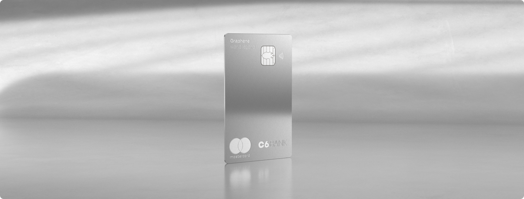 Fotografia do cartão C6 Graphene World Legend Mastercard em fundo prata reflexivo.